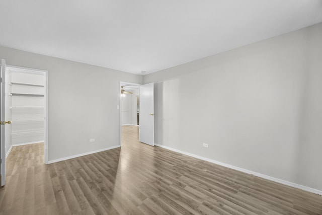 unfurnished bedroom with a spacious closet, a closet, baseboards, and wood finished floors