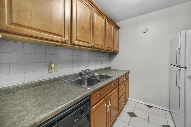 kitchen featuring dark countertops, decorative backsplash, freestanding refrigerator, brown cabinetry, and a sink