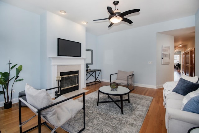 living area featuring a fireplace with flush hearth, wood finished floors, baseboards, and ceiling fan