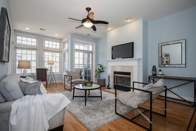 living area featuring visible vents, baseboards, a tile fireplace, wood finished floors, and a ceiling fan