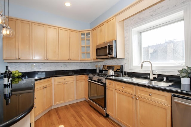 kitchen with light brown cabinets, appliances with stainless steel finishes, dark countertops, and a sink