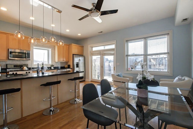 kitchen featuring a kitchen bar, light brown cabinetry, dark countertops, appliances with stainless steel finishes, and ceiling fan