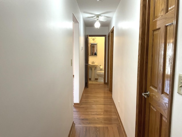 hall with light wood-type flooring, baseboards, and a sink