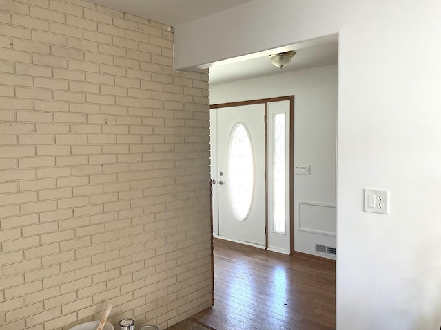 foyer with visible vents, dark wood-style floors, and brick wall