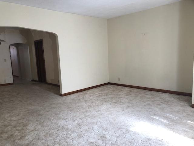 carpeted empty room featuring baseboards and arched walkways