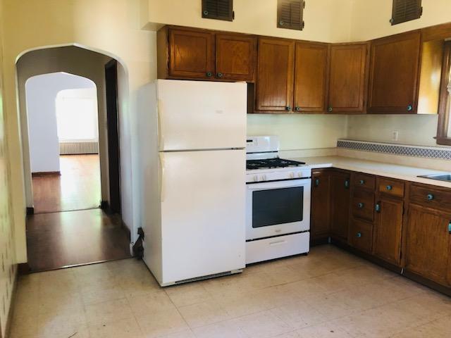 kitchen featuring visible vents, radiator heating unit, light countertops, arched walkways, and white appliances