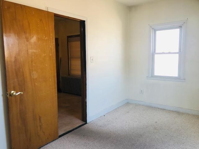 carpeted empty room with radiator and baseboards