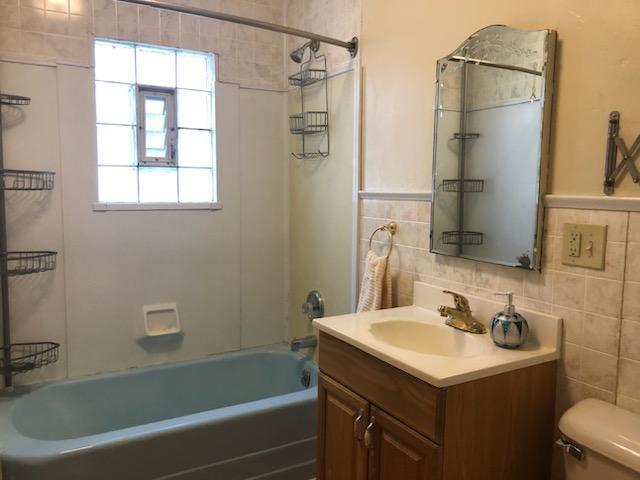 bathroom with shower / bath combination, toilet, tile walls, and vanity