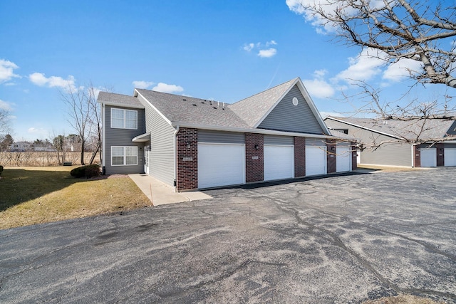 view of home's exterior with a lawn, aphalt driveway, an attached garage, a shingled roof, and brick siding