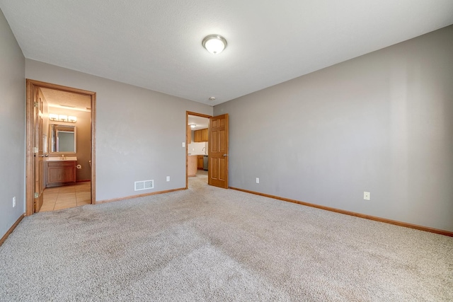 unfurnished bedroom with connected bathroom, light colored carpet, visible vents, and baseboards