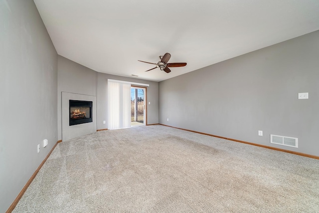 unfurnished living room with visible vents, a warm lit fireplace, carpet flooring, baseboards, and ceiling fan