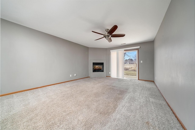 unfurnished living room with a lit fireplace, carpet flooring, baseboards, and a ceiling fan