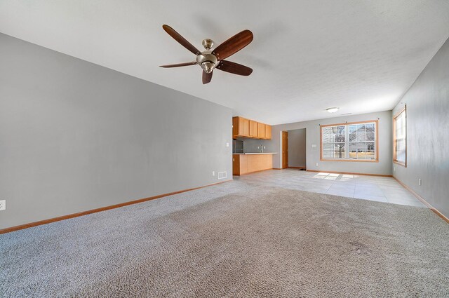 unfurnished living room featuring visible vents, light carpet, a ceiling fan, light tile patterned floors, and baseboards