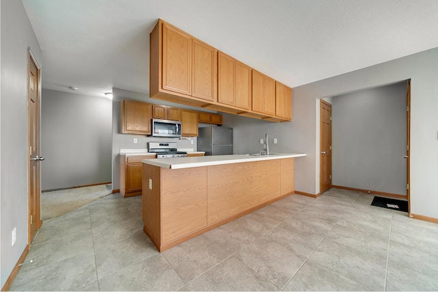 kitchen featuring baseboards, light countertops, appliances with stainless steel finishes, a peninsula, and a sink