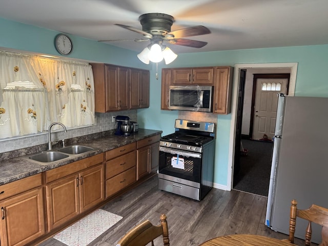 kitchen featuring dark countertops, backsplash, dark wood finished floors, stainless steel appliances, and a sink