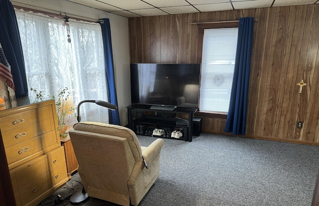 carpeted living room with a paneled ceiling and wood walls