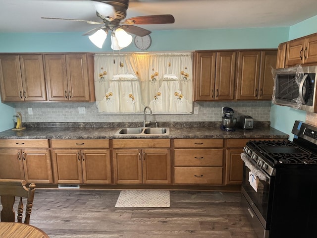 kitchen with brown cabinetry, a sink, dark wood-type flooring, appliances with stainless steel finishes, and dark countertops