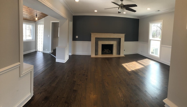 unfurnished living room featuring a ceiling fan, a wainscoted wall, a healthy amount of sunlight, and dark wood finished floors