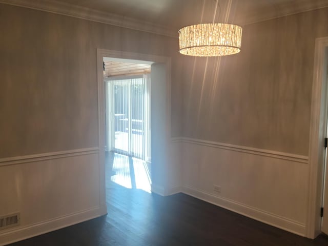 unfurnished dining area with a notable chandelier, dark wood-type flooring, visible vents, and ornamental molding