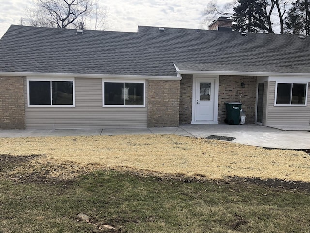 rear view of house featuring a patio, a yard, brick siding, and roof with shingles