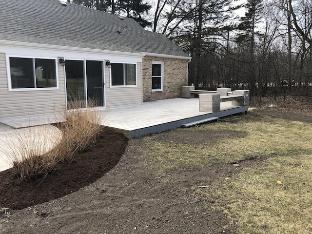 exterior space with brick siding, roof with shingles, cooling unit, a deck, and a yard