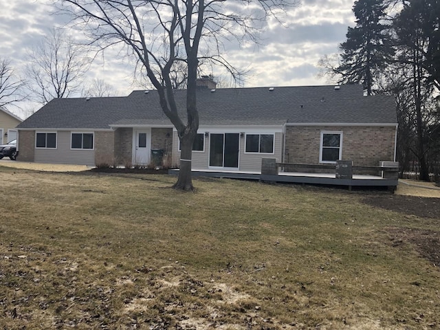 rear view of property featuring a yard, brick siding, roof with shingles, and a wooden deck