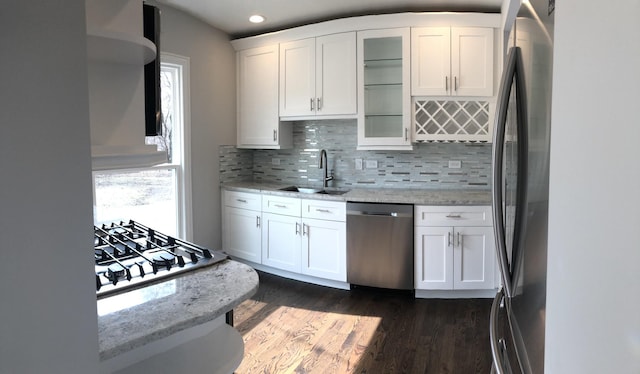 kitchen with light stone counters, a sink, stainless steel appliances, white cabinets, and glass insert cabinets