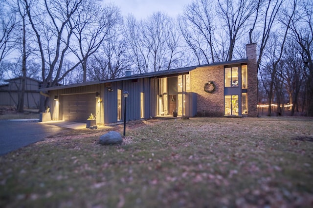 mid-century inspired home with brick siding, a garage, driveway, and a chimney