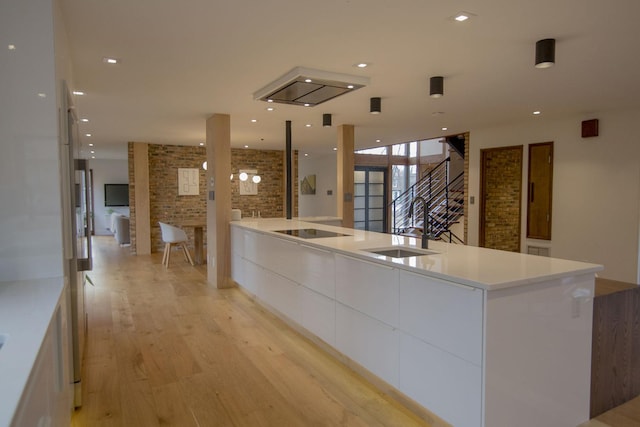 kitchen featuring brick wall, black electric stovetop, light wood-style floors, white cabinets, and modern cabinets