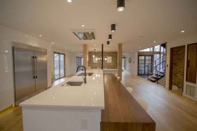 kitchen featuring light wood finished floors, a sink, stainless steel built in fridge, white cabinetry, and modern cabinets