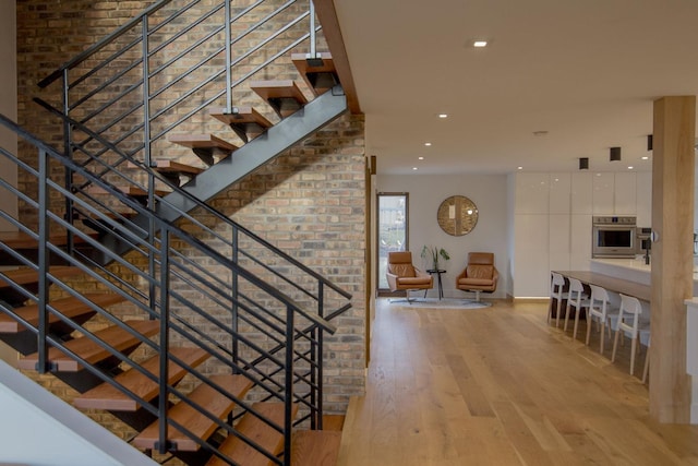 staircase with recessed lighting, wood finished floors, and brick wall