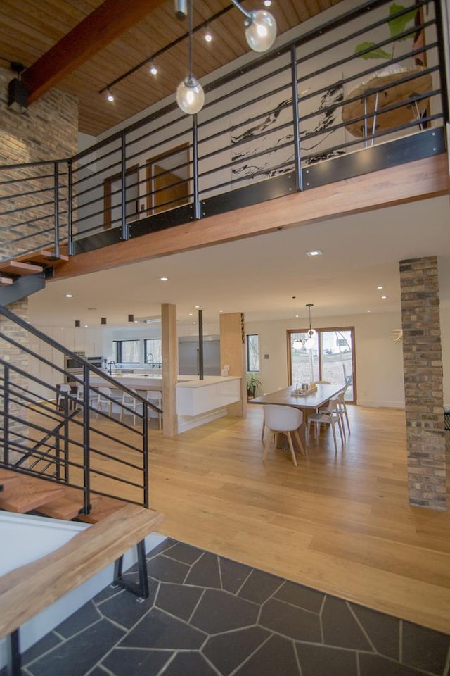 stairway featuring beam ceiling, wood finished floors, wood ceiling, a towering ceiling, and ornate columns