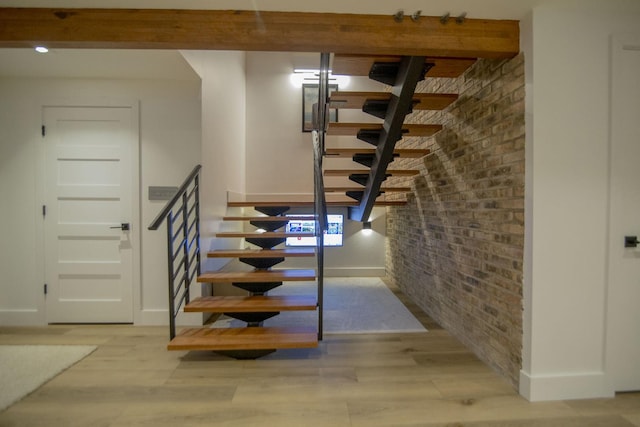 stairway featuring wood finished floors, baseboards, and brick wall