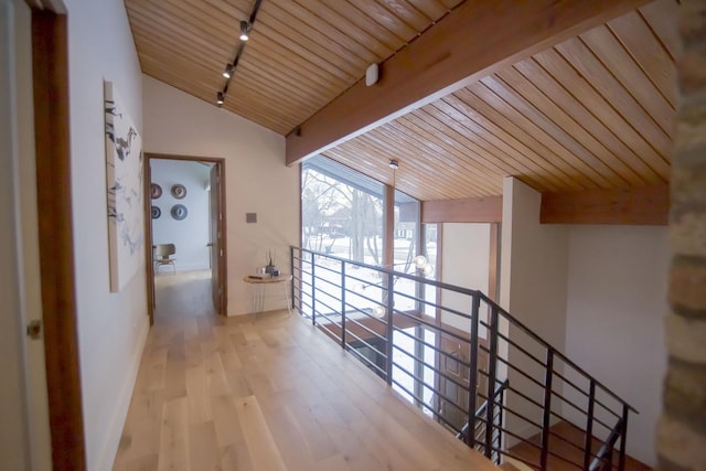 hallway with an upstairs landing, lofted ceiling with beams, wood finished floors, rail lighting, and wood ceiling