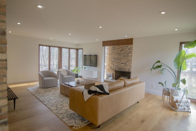 living room with a wealth of natural light, light wood-style floors, a brick fireplace, and recessed lighting