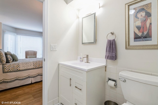 bathroom featuring toilet, ensuite bathroom, wood finished floors, tile walls, and vanity