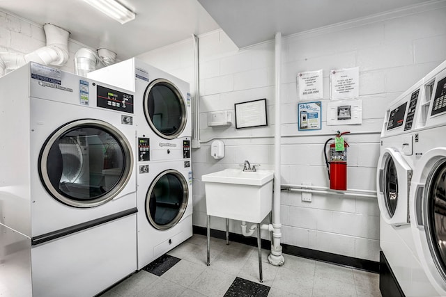 shared laundry area featuring a sink, stacked washer / dryer, concrete block wall, and washer and clothes dryer