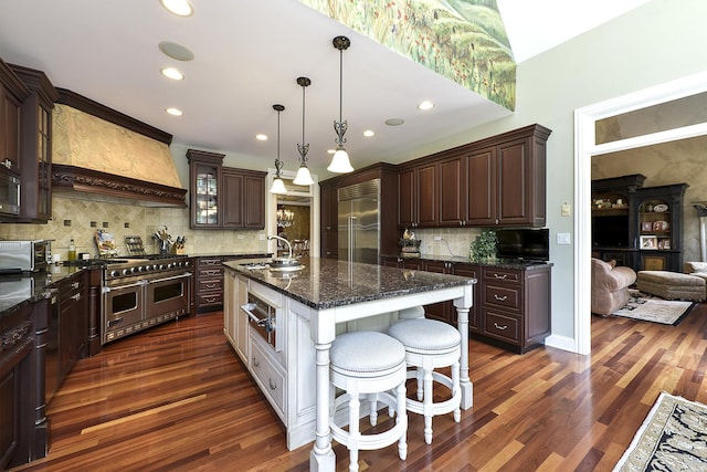 kitchen with dark wood finished floors, dark brown cabinetry, custom range hood, premium appliances, and a sink