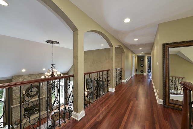 hallway with arched walkways, a notable chandelier, baseboards, and wood finished floors