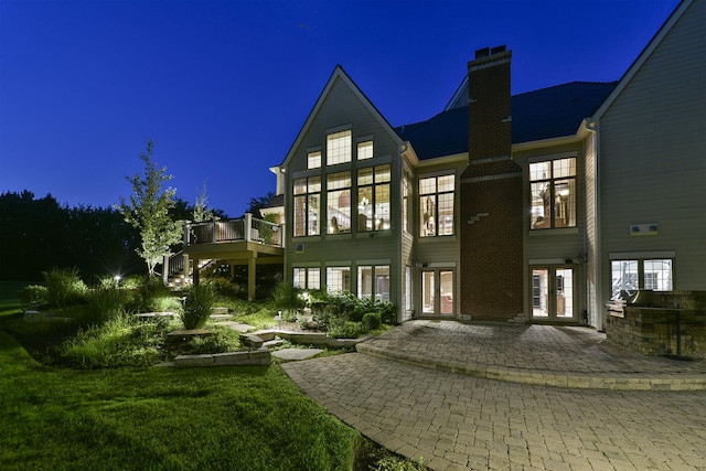 back of house at night with a patio, exterior kitchen, a chimney, french doors, and a deck