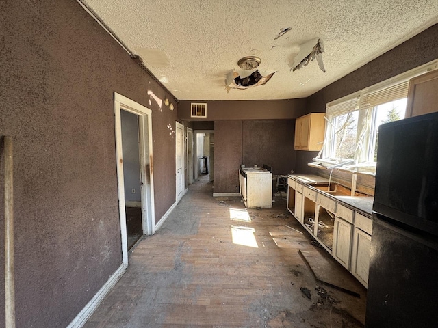 kitchen featuring visible vents, a textured ceiling, freestanding refrigerator, and baseboards