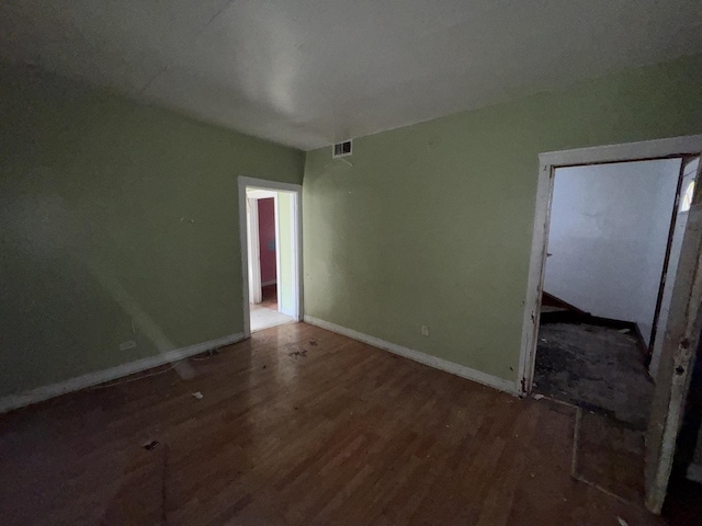 spare room featuring wood finished floors, visible vents, and baseboards