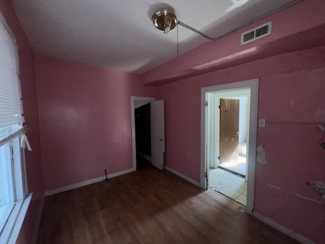 empty room with wood finished floors, visible vents, and baseboards