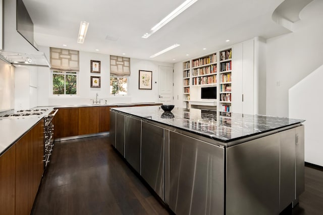 kitchen featuring dark wood-style flooring, brown cabinets, modern cabinets, wall chimney exhaust hood, and a sink