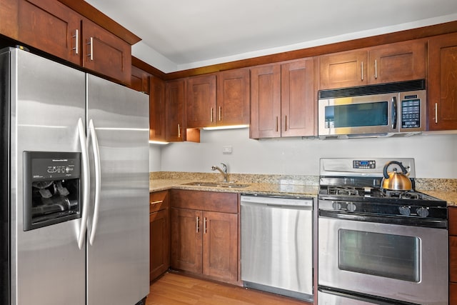 kitchen with light stone counters, brown cabinetry, a sink, appliances with stainless steel finishes, and light wood-type flooring