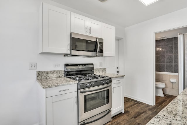 kitchen with dark wood-type flooring, white cabinets, light stone counters, and appliances with stainless steel finishes