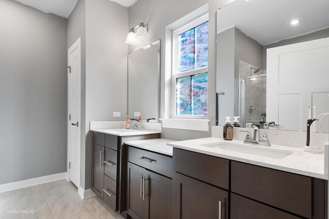 full bath with a shower stall, two vanities, baseboards, and a sink