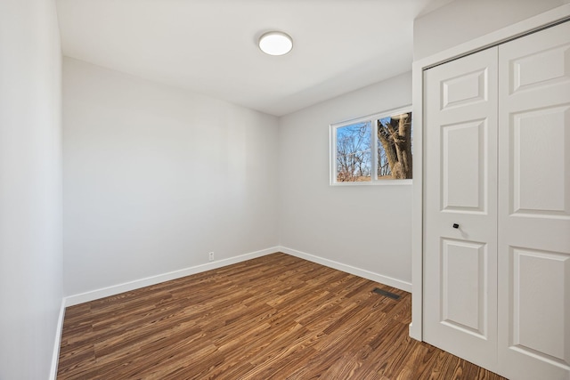 unfurnished bedroom with a closet, baseboards, visible vents, and dark wood finished floors