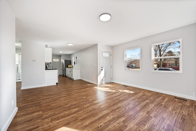 unfurnished living room with dark wood-style floors, visible vents, and baseboards