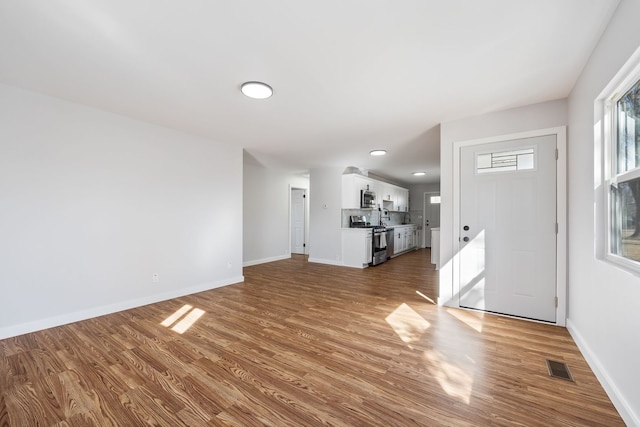 unfurnished living room with visible vents, baseboards, and wood finished floors